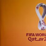 A man smoking next to the logo of the Qatar 2022 FIFA World Cup football tournament is displayed on a wall in Doha on October 23, 2022. | Photo Credit: AFP