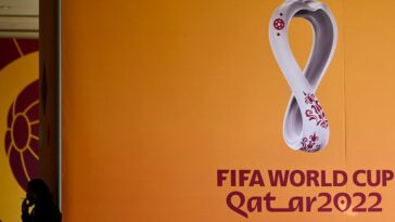 A man smoking next to the logo of the Qatar 2022 FIFA World Cup football tournament is displayed on a wall in Doha on October 23, 2022. | Photo Credit: AFP
