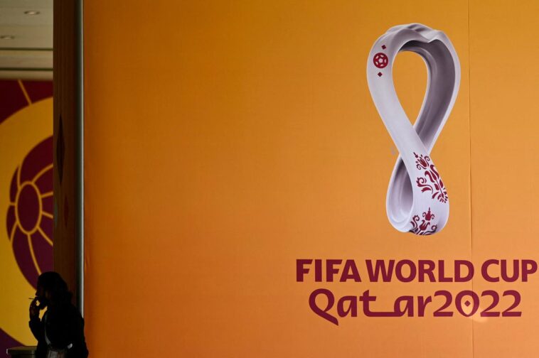 A man smoking next to the logo of the Qatar 2022 FIFA World Cup football tournament is displayed on a wall in Doha on October 23, 2022. | Photo Credit: AFP
