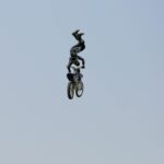 Daring motocross stunt rider performing aerial tricks on motorcycle against clear sky.