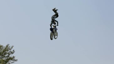 Daring motocross stunt rider performing aerial tricks on motorcycle against clear sky.