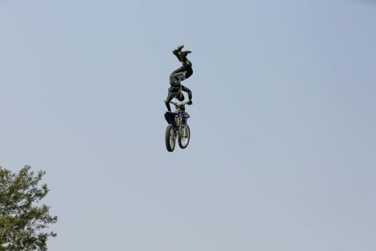 Daring motocross stunt rider performing aerial tricks on motorcycle against clear sky.