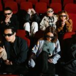Group of people watching a movie in 3D glasses, expressing excitement and surprise.