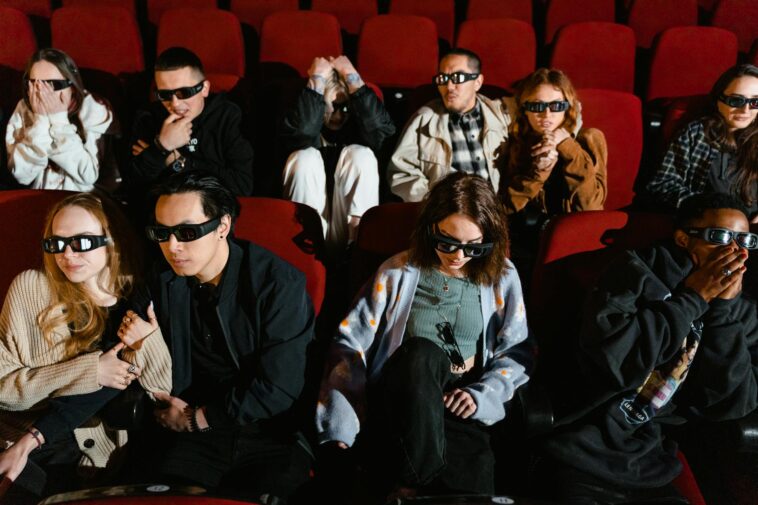 Group of people watching a movie in 3D glasses, expressing excitement and surprise.