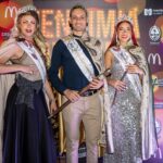 Three pageant winners pose in elegant attire with crowns and sashes at a vibrant event.