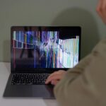 Individual viewing a laptop displaying a cracked and colorful digital screen indoors.