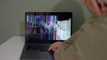 Individual viewing a laptop displaying a cracked and colorful digital screen indoors.