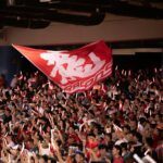 Vibrant crowd waving a flag with glowing sticks at a Taipei sports event, showcasing excitement and unity.