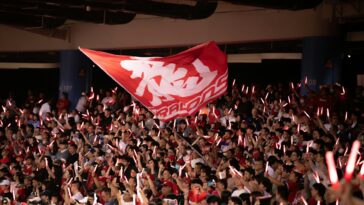 Vibrant crowd waving a flag with glowing sticks at a Taipei sports event, showcasing excitement and unity.