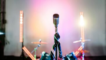 Retro microphone on a stage with colorful lights and a drum set, perfect for music themes.