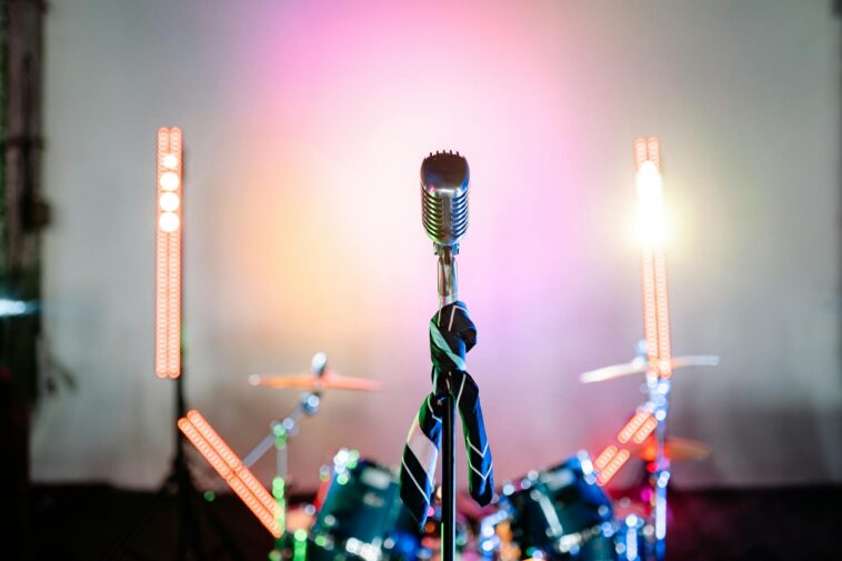 Retro microphone on a stage with colorful lights and a drum set, perfect for music themes.