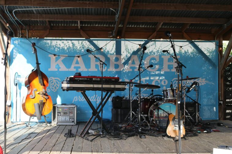 An outdoor stage with various musical instruments including a cello, drum set, and keyboard.