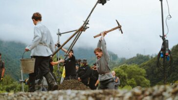 Film crew setting up a historical scene with actors outdoors in nature.