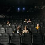 Image of diverse audience sparsely seated in a dimly lit cinema hall.