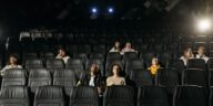 Image of diverse audience sparsely seated in a dimly lit cinema hall.