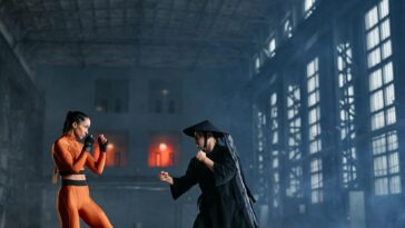 Two cosplayers in dynamic fighting pose inside industrial building.