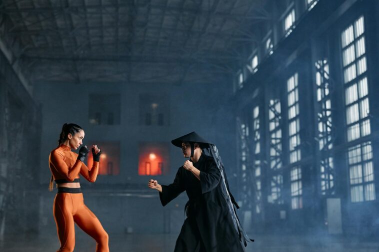 Two cosplayers in dynamic fighting pose inside industrial building.