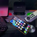 Stylish home entertainment setup featuring an iPhone, Apple TV, and gaming controller on a dark surface.