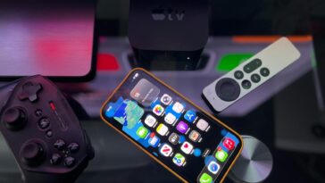 Stylish home entertainment setup featuring an iPhone, Apple TV, and gaming controller on a dark surface.