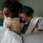 Two women sharing an emotional moment while watching a movie at home, enjoying popcorn.