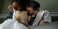 Two women sharing an emotional moment while watching a movie at home, enjoying popcorn.