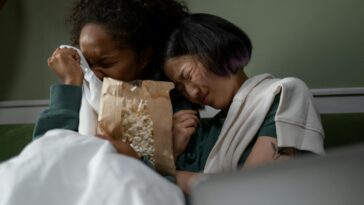 Two women sharing an emotional moment while watching a movie at home, enjoying popcorn.