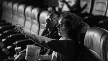 A couple laughing and enjoying a movie in a dimly lit theater, sharing popcorn.