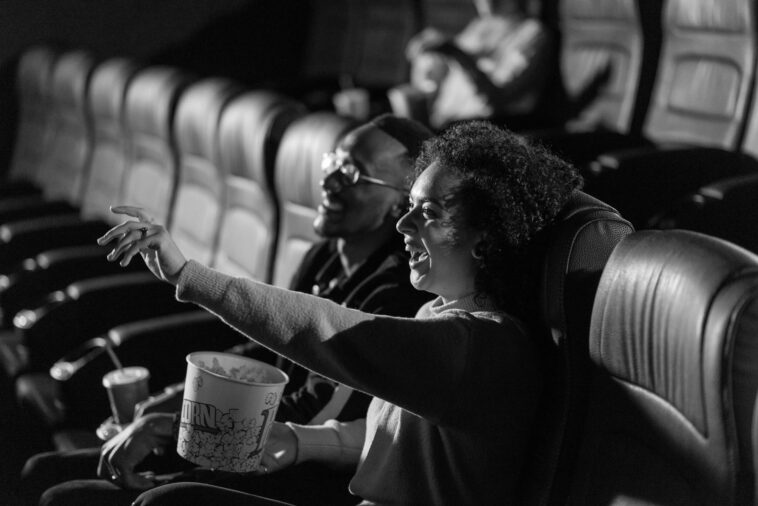 A couple laughing and enjoying a movie in a dimly lit theater, sharing popcorn.