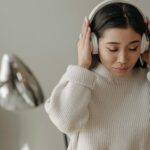 Asian woman wearing headphones and a knitted sweater, enjoying music indoors.