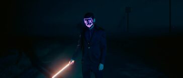 Dark night scene of a mysterious figure in a glowing mask holding a light sword.