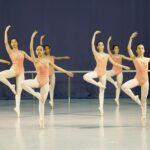 Group of young ballet dancers practicing with arms raised in a dance studio.