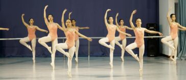 Group of young ballet dancers practicing with arms raised in a dance studio.