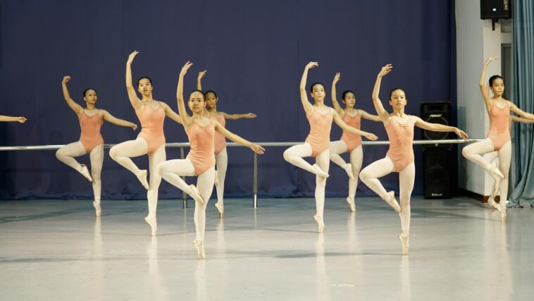 Group of young ballet dancers practicing with arms raised in a dance studio.