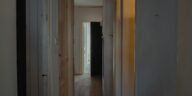 A dimly lit hallway in an apartment with wooden doors and a rustic feel.
