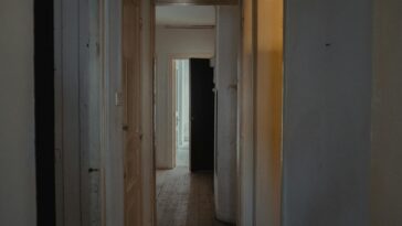 A dimly lit hallway in an apartment with wooden doors and a rustic feel.