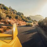 Three yellow sports cars speeding on a scenic mountain road at sunset, creating a thrilling and dynamic scene.