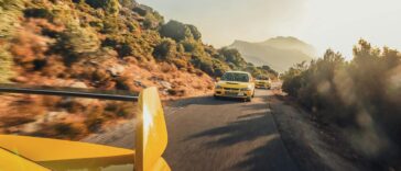 Three yellow sports cars speeding on a scenic mountain road at sunset, creating a thrilling and dynamic scene.