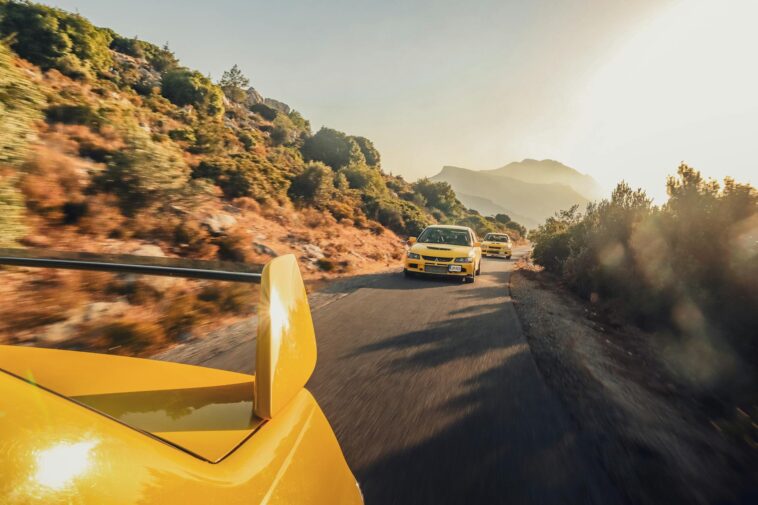 Three yellow sports cars speeding on a scenic mountain road at sunset, creating a thrilling and dynamic scene.