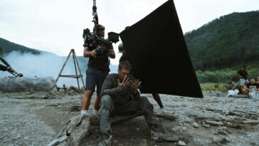 Behind-the-scenes view of film production with actors and crew on location outdoors.