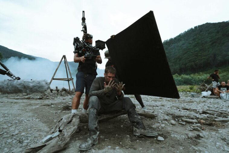 Behind-the-scenes view of film production with actors and crew on location outdoors.