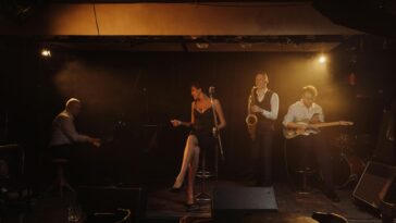 A jazz band performing with a female singer and musicians playing piano, saxophone, and guitar on stage.