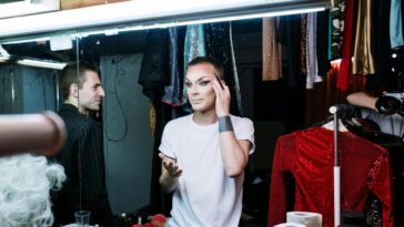 A drag queen applying makeup backstage, showcasing transformation and self-expression.