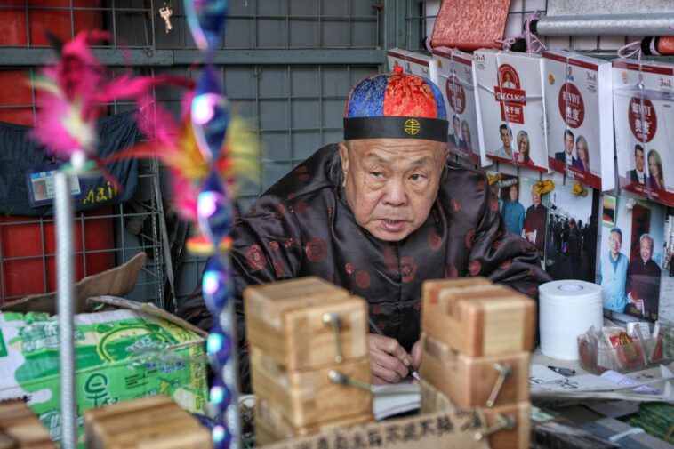 Elderly man in traditional attire working at a market stall in Beijing, China.