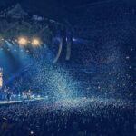 Energetic live concert with confetti and cheering crowd under bright stage lights.