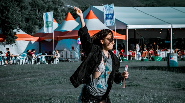 A woman joyfully plays with bubbles at an outdoor festival.