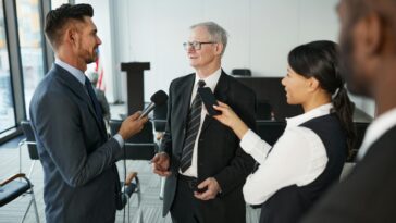 Journalists conduct an interview with a senior executive in a formal office setting.