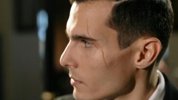 Close-up portrait of a man with a scar, exuding mystery and intrigue in a low-light setting.