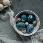 A collection of artistically dyed Easter eggs in a bowl, set on a textured concrete surface with rustic decor.