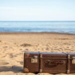 A vintage brown suitcase sits on a sandy beach, evoking travel and adventure.