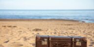 A vintage brown suitcase sits on a sandy beach, evoking travel and adventure.